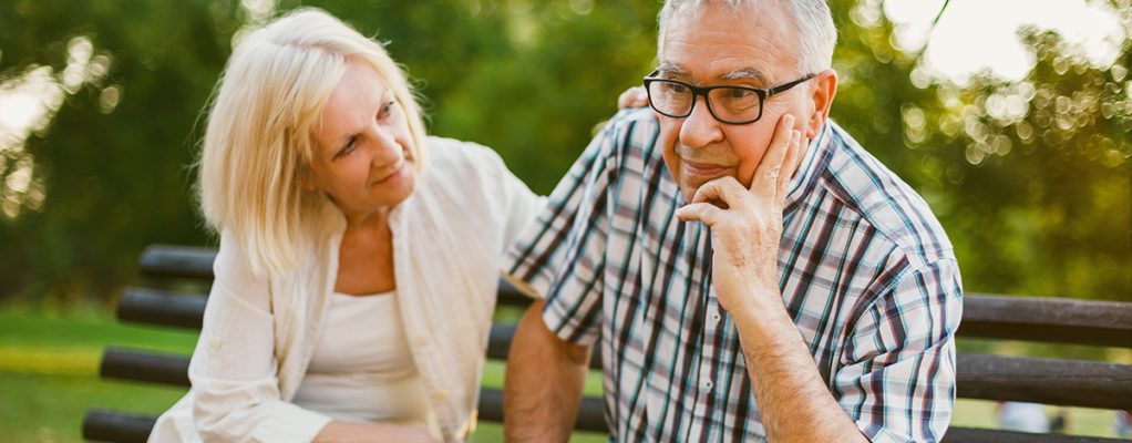elderly couple sitting on bench looking concerned