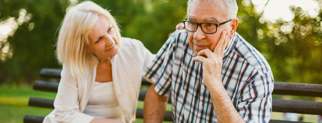 elderly couple sitting on bench looking concerned