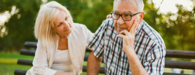 elderly couple sitting on bench looking concerned