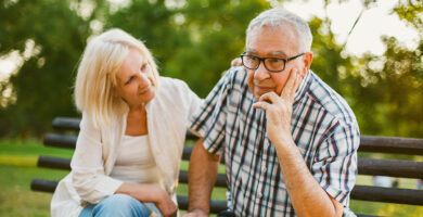 elderly couple sitting on bench looking concerned