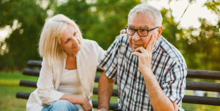 elderly couple sitting on bench looking concerned