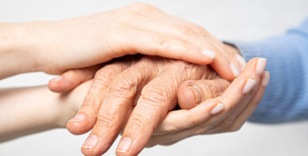 a younger person holds the hands of an older person
