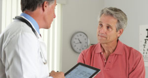 A doctor holds an iPad and talks to a male patient
