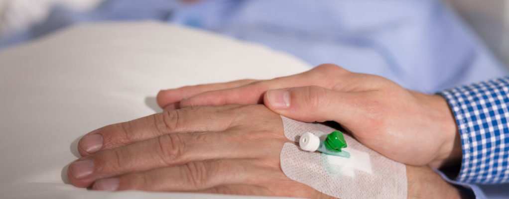 someone puts their hand on the hand of an older man in bed