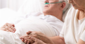 A woman holds a loved one's hand at bedside