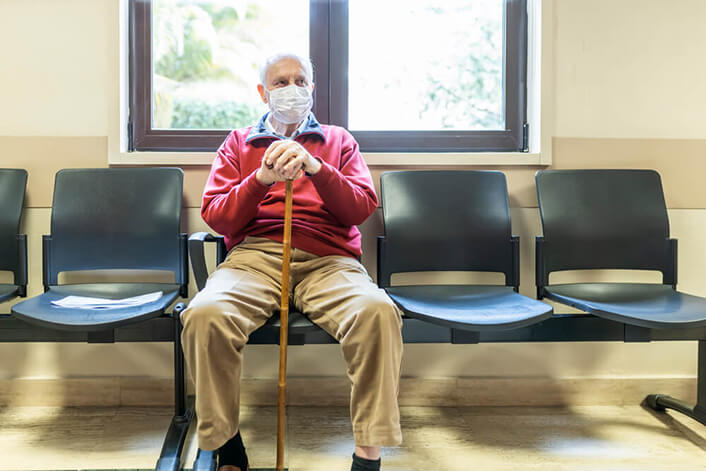An elderly man in a mask sits in a waiting room