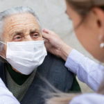 A woman puts a surgical mask on the face of an elderly patient