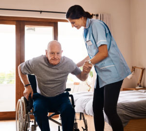 An in-home aide helps an elderly man get seated in his wheelchair 