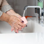 An elderly woman washes her hands with a bar of soap
