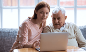 Woman helping an elderly man research mesothelioma doctors on a laptop computer