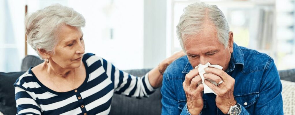 Man blowing his nose whole woman comforts him