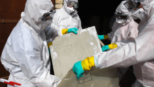 Two workers in hazmat suits remove some asbestos