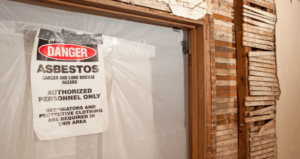 An asbestos danger sign posted on the door of a dilapidated building