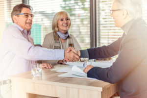 Lawyer shakes hands with a man and his wife after a successful mesothelioma settlement