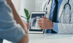 A doctor holds up an iPad and shows it to a patient