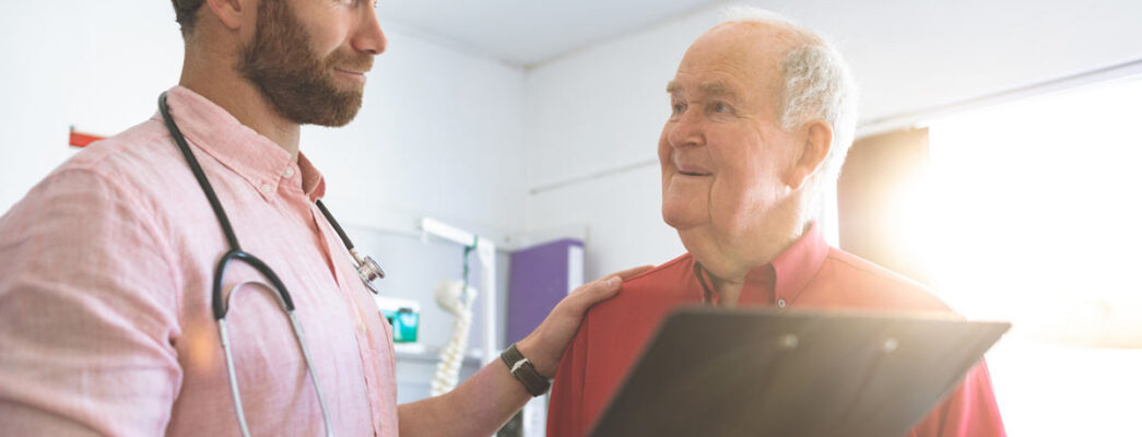 A male doctor puts his hand on the shoulder of an older male patient