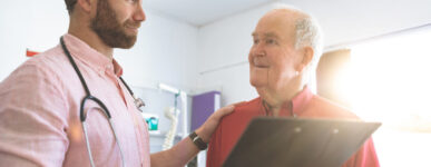 A male doctor puts his hand on the shoulder of an older male patient