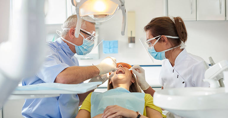 Two dentists examine a young patient's mouth in a white office