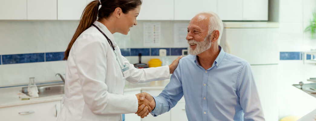 A doctor shakes a male patient's hand and pats him on the shoulder with her other hand