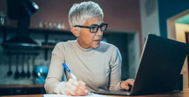 Woman looking at her laptop and writing with a pen and paper