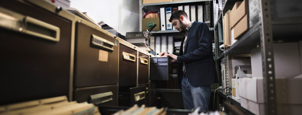 An office worker reviews a set of documents from a row of metal filing cabinets
