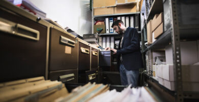 An office worker reviews a set of documents from a row of metal filing cabinets