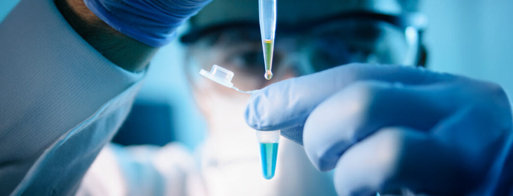 A lab technical uses a dropper to add liquid to a test vial