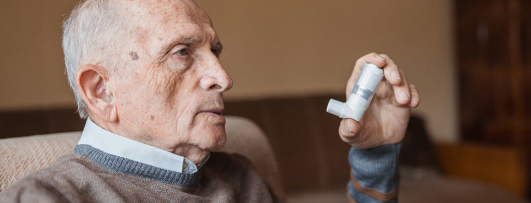 Elderly man holding an inhaler in one hand