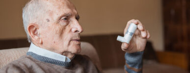 Elderly man holding an inhaler in one hand